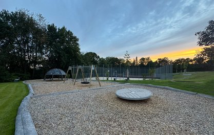 Spielgeräte zum Klettern, Schaukeln und eine Drehscheibe, im Hintergrund ein beachplatz und ein Tenniscourt