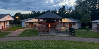 Grillhütte mit loderndem Feuer in der Mitte von vier Blockhäusern 