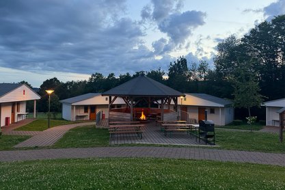 Grillhütte mit loderndem Feuer in der Mitte von vier Blockhäusern 