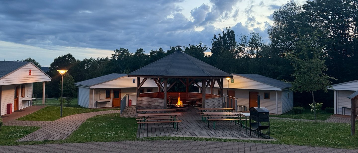 Grillhütte mit loderndem Feuer in der Mitte von vier Blockhäusern 